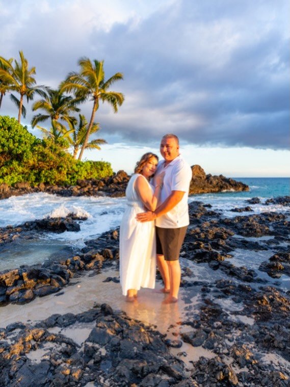 A couple on the lava rocks with palms and ocean behind them
