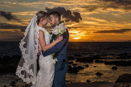 A Maui bride with bridal hair and makeup beside her groom on the beach